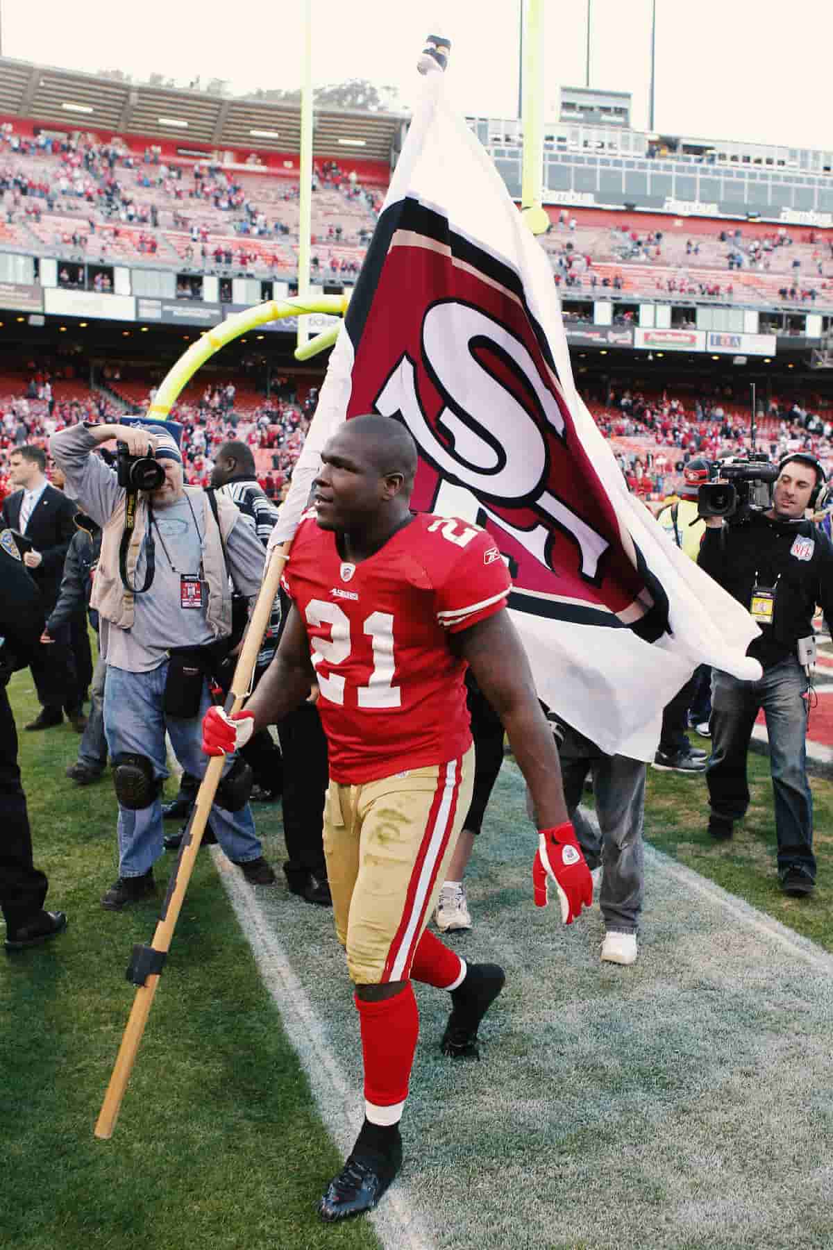 Frank Gore flies a San Fransisco 49ers flag in front of a stadium of cheering fans.